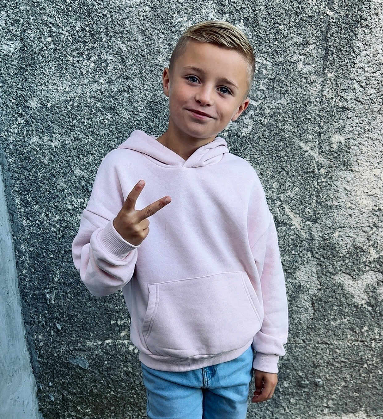 Mathis a rejoint le concours — aidez-le/la à gagner de superbes lots ! child, boy, peace_sign, hoodie, light_pink, blue_jeans, smile, casual_clothing, urban, wall, texture, portrait, standing, young, outdoor, cool, confident, person, fashion, casual