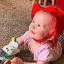 baby, red_hat, pink_shirt, carpet, plush_toy, child, indoor, smiling, cute, infant, happy, playing, young_child, blue_eyes, soft_toys, floor, person, headwear, expression, toddler