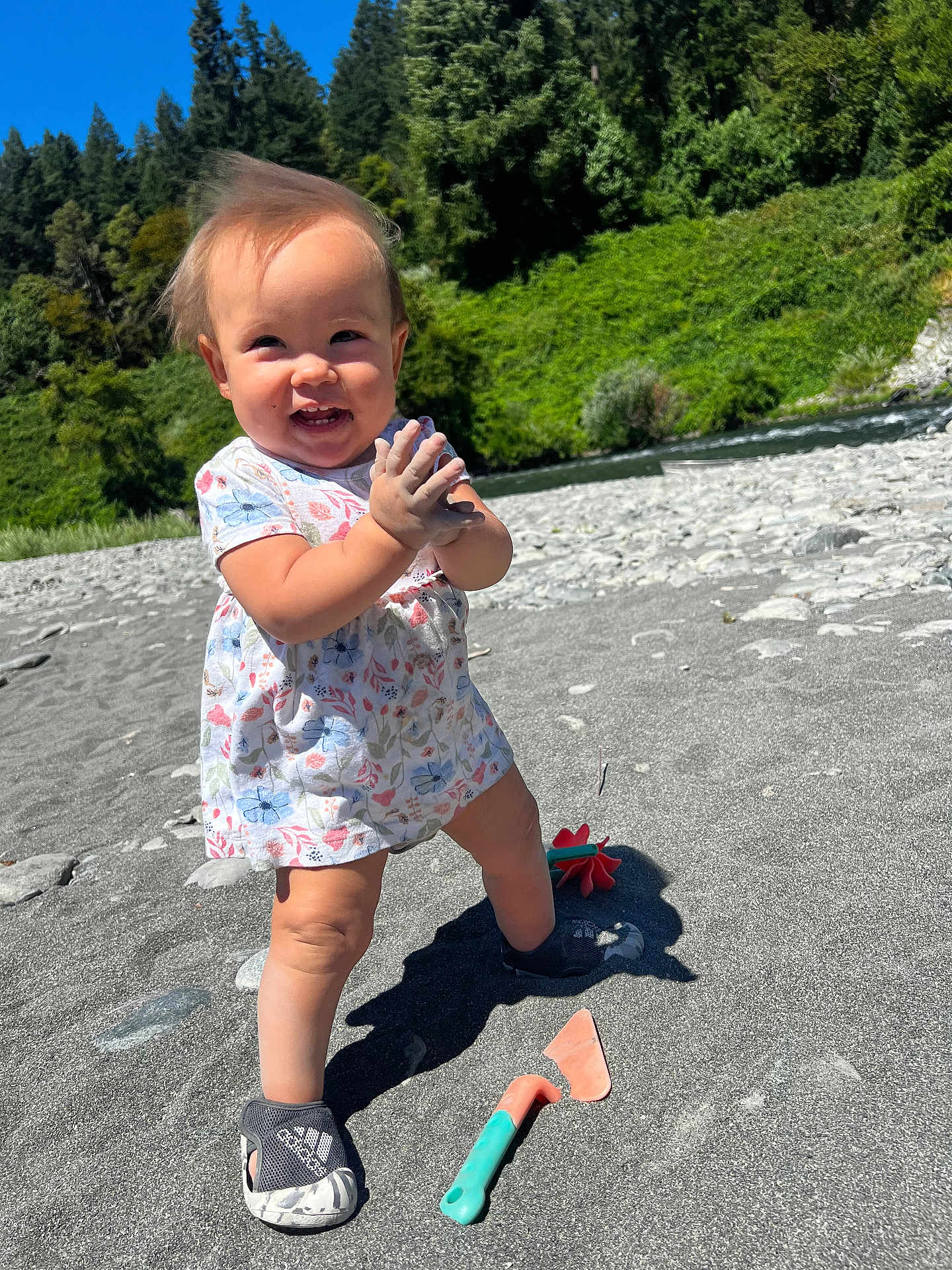 Kalina is registered to the contest to win money with this photo: toddler, child, smiling, outdoor, beach, sand, rocks, toys, dress, shoes, sunny, nature, trees, river, clapping, happy, daytime, play, baby, person