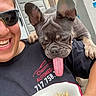 person, dog, french_bulldog, tongue_out, sunglasses, smiling, bowl, food, porch, stairs, door, happy, pet, outdoor, casual, black_shirt, short_hair, playful, animal, companion