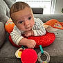 baby, child, infant, couch, toy, orange, gray, striped_clothing, indoor, curious, face, hand, plush, window, light, person, soft_toy, colorful, resting, expression