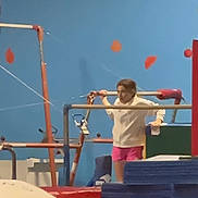 Izzy is registered to the contest to win money with this photo: child, gymnastics, gymnastics_bars, indoor, blue_wall, red_padding, stacked_mats, pink_shorts, white_top, exercise, sport, training, young, person, activity, equipment, fitness, balance, concentration, candid