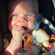 ély a rejoint le concours — aidez-le/la à gagner de superbes lots ! baby, blue_eyes, pacifier, toy, plush, hand, face, infant, sunlight, close_up, cute, child, fingertip, soft_toy, expression, chewing, indoor, car_seat, bright, adorable