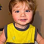 toddler, child, smiling, yellow_shirt, blonde_hair, blue_eyes, indoor, sitting, tank_top, graphic_tshirt, cute, happy, face, person, shorts, playful, young_child, casual_clothing, portrait, closeup