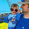 toddler, child, man, sunglasses, cap, blue_shirt, outdoor, sunny, canopy, grass, smile, hand, face, clothing, holding, portrait, daylight, hat, happy, family