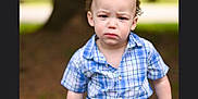 Jay joined the competition — help win amazing prizes! blue_shirt, casual_clothing, child, curly_hair, daylight, frown, greenery, nature, outdoor, park, person, plaid_shirt, portrait, rock, serious_expression, shorts, sitting, toddler, tree, young_child