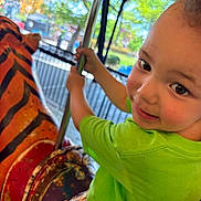 Jay joined the competition — help win amazing prizes! amusement_park, carousel, child, daylight, face, fence, fun, green_shirt, metal, outdoor, plaid_shorts, playful, pole, portrait, ride, rustic, smiling, tiger, toddler, vintage