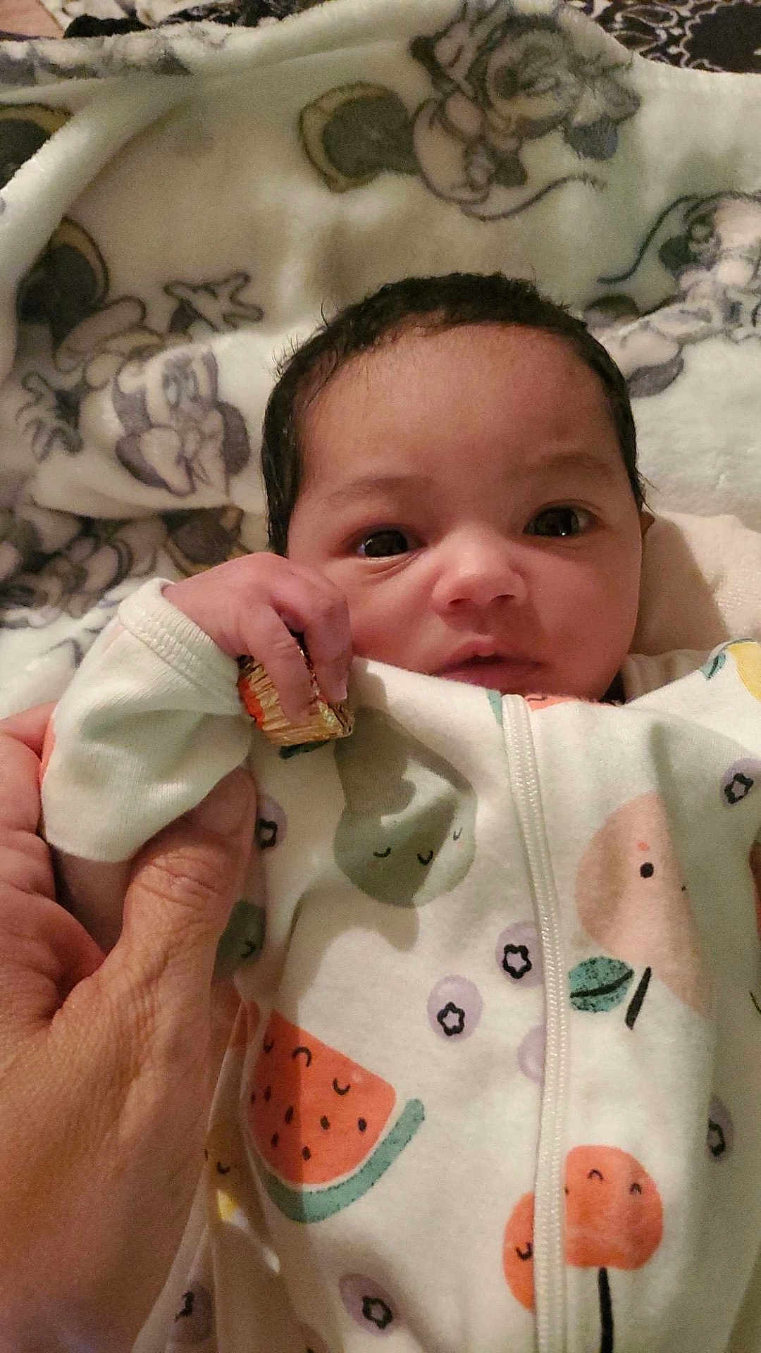 Nova is registered to the contest to win money with this photo: baby, infant, hand, blanket, onesie, fruit_pattern, cute, clothing, holding, person, face, expression, indoors, soft_toys, comfort, newborn, sleepwear, skin, adult_hand, portrait