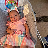 Naomi is registered to the contest to win money with this photo: baby, child, smiling, happy, pink_clothing, headband, bow, baby_seat, indoor, floor, tile_floor, colorful, rainbow, elephant, monkey, sun, toy_design, cute, infant, portrait