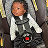 baby, car_seat, child, curly_hair, black_pants, white_shirt, safety_harness, infant, seat_belt, indoors, serious_expression, young_child, fabric, warning_label, soft_texture, footwear, black_socks, closeup, person, resting