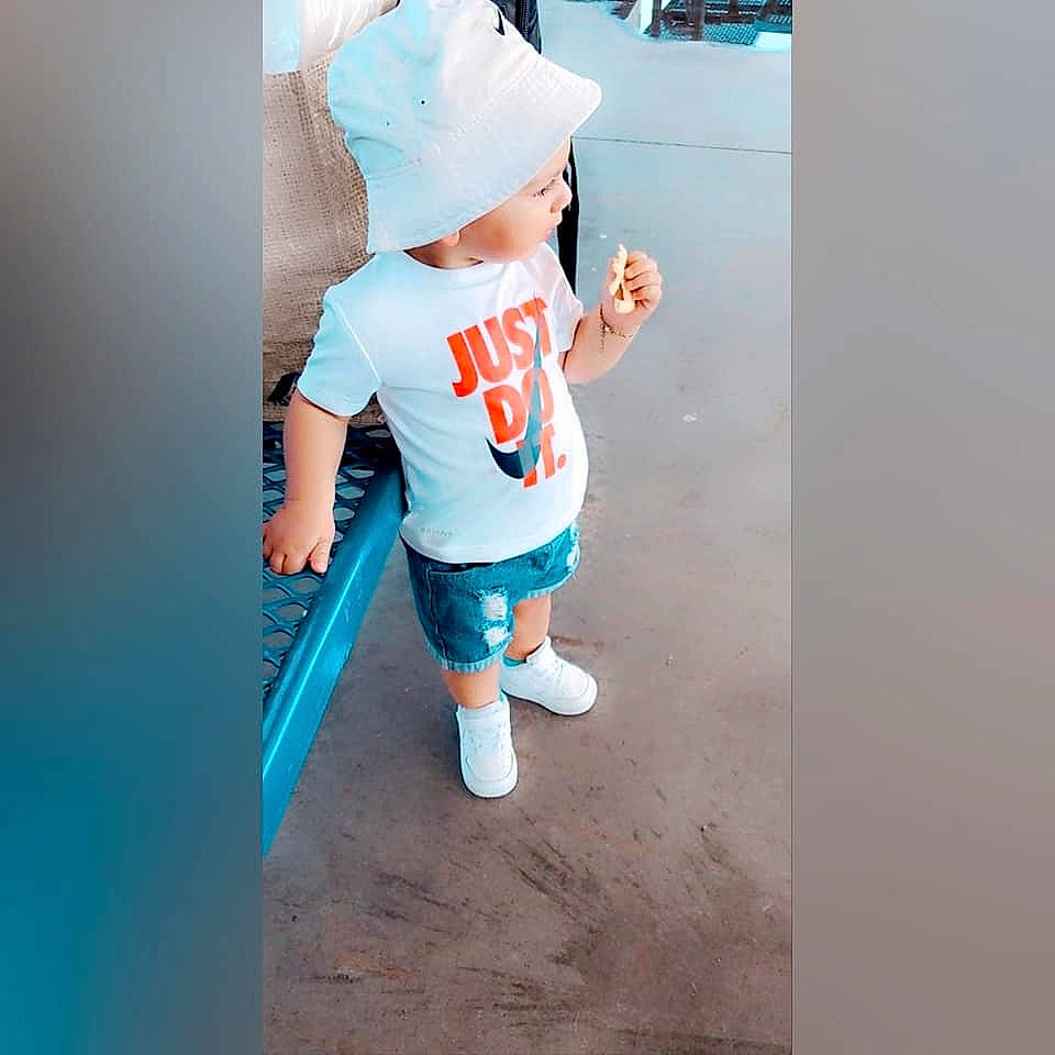 Liam is registered to the contest to win money with this photo: baby, baby_toddler_clothing, baseball_cap, blue, cap, denim, electric_blue, fictional_character, gesture, happy, hat, headwear, human_leg, knee, person, shorts, sleeve, sock, sportswear, t_shirt