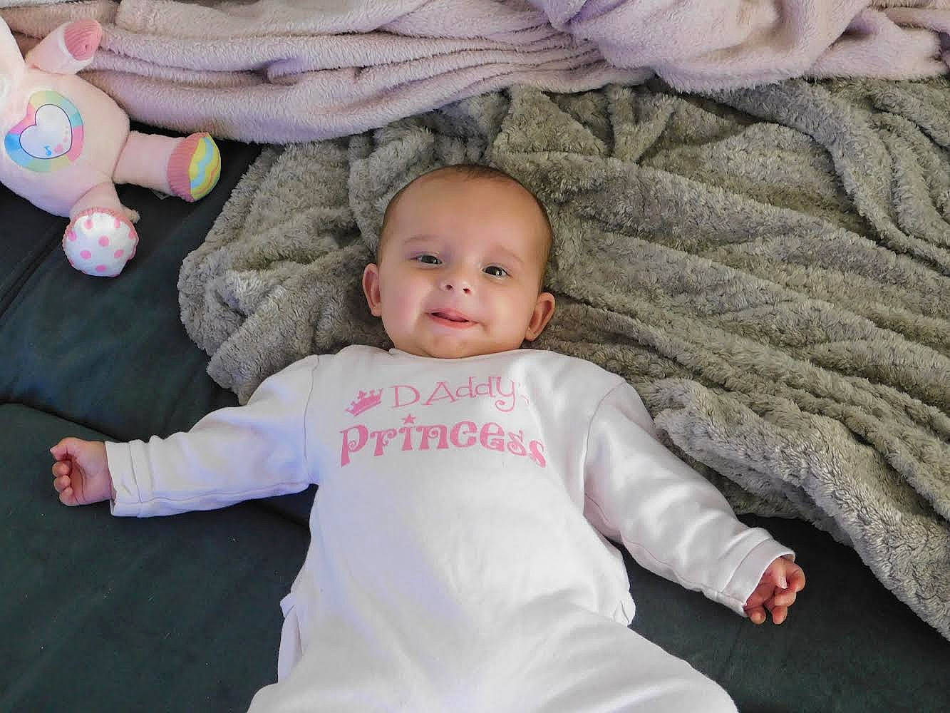 Anaë participe au concours pour gagner de l'argent avec cette photo : baby, baby_toddler_clothing, cheek, comfort, eye, finger, gesture, hand, happy, head, iris, joy, nose, person, pink, skin, sleeve, smile, textile, thumb