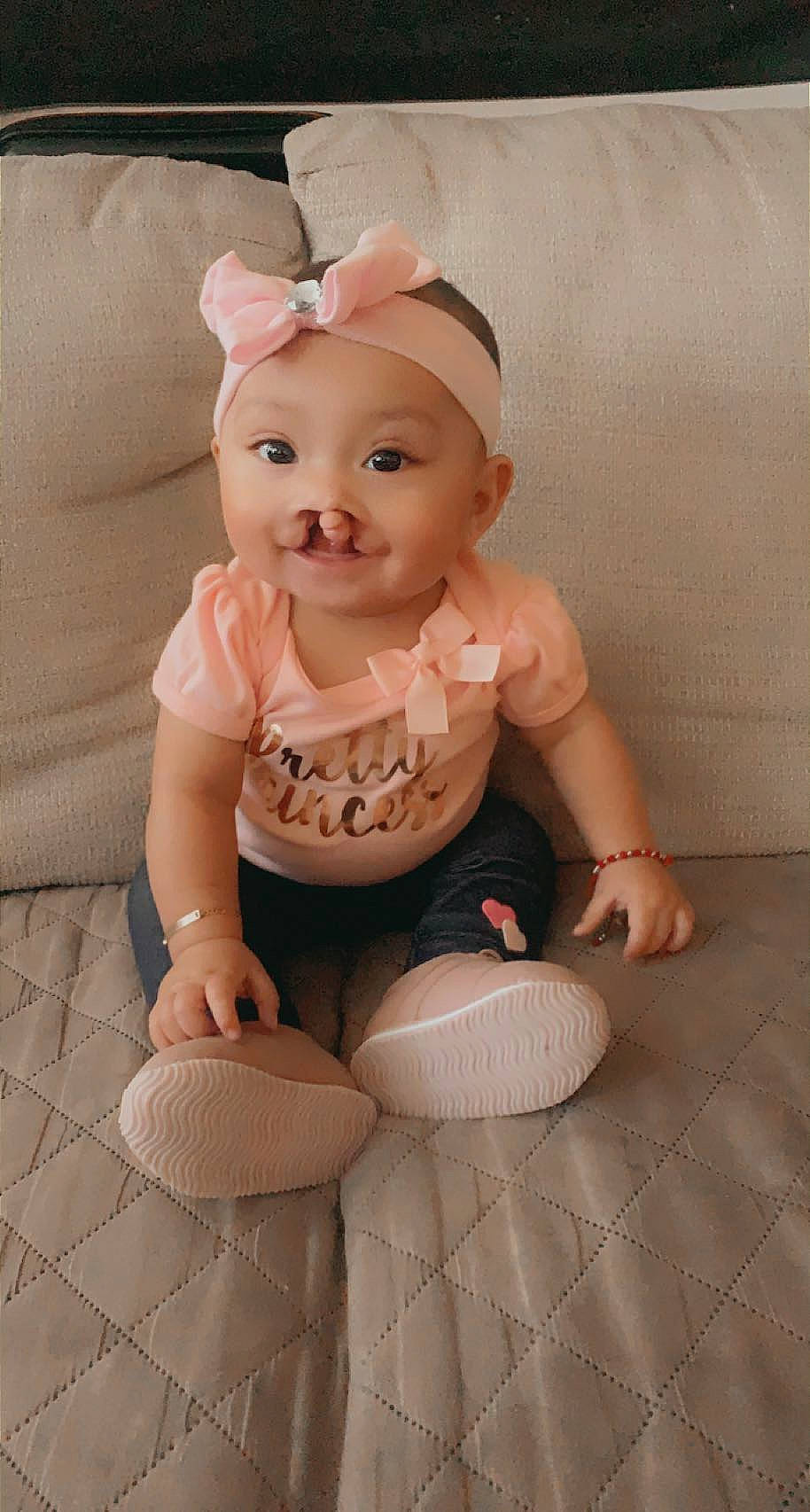 Emiliana is registered to the contest to win money with this photo: arm, baby, baby_toddler_clothing, cheek, chin, dress, eye, floor, flooring, headgear, headwear, human_body, iris, joy, lip, mouth, person, pink, sitting, skin