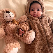 Darian is registered to the contest to win money with this photo: baby, teddy_bear, plush_toy, bed, blanket, soft_texture, onesie, cute, infant, child, smile, face, hand, lying_down, cozy, warm_clothing, indoors, portrait, fuzzy, adorable