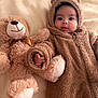 baby, teddy_bear, plush_toy, bed, blanket, soft_texture, onesie, cute, infant, child, smile, face, hand, lying_down, cozy, warm_clothing, indoors, portrait, fuzzy, adorable