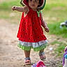 Camille is registered to the contest to win money with this photo: toddler, child, jumping, red_dress, watermelon_pattern, sunhat, outdoor, playground, toy, unicorn, sandals, grass, blurred_background, cute, playful, person, summer, hat, colorful, walking