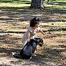 child, dog, outdoor, park, tree, grass, sunlight, shadow, picnic_table, curly_hair, dress, petting, animal, nature, playful, friendship, summer, young_child, canine, leash