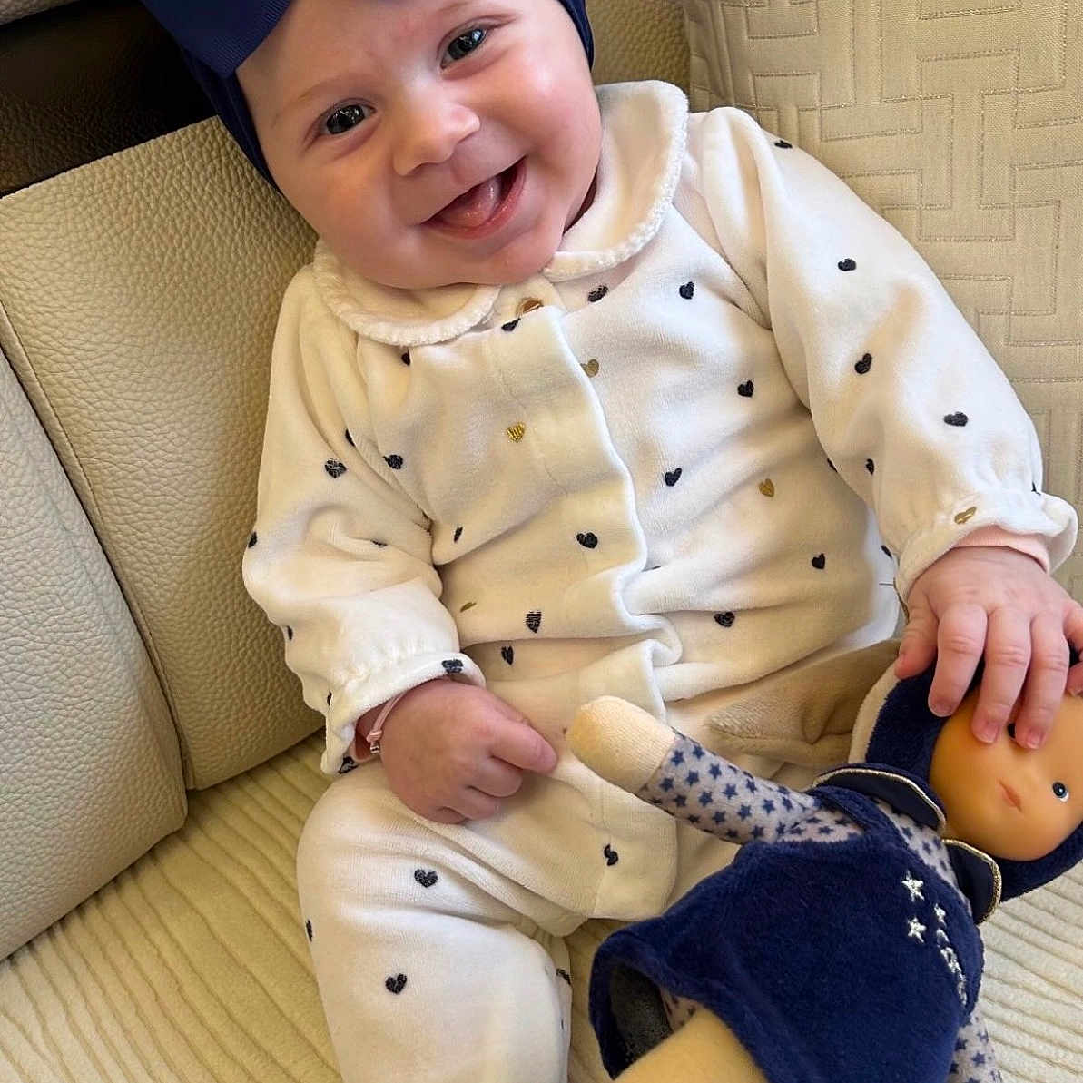 Noa a rejoint le concours — aidez-le/la à gagner de superbes lots ! baby, smiling, infant, headband, bow, doll, couch, cushion, white_clothing, heart_pattern, indoor, child, cute, happy, seated, toy, soft_toy, portrait, person, home
