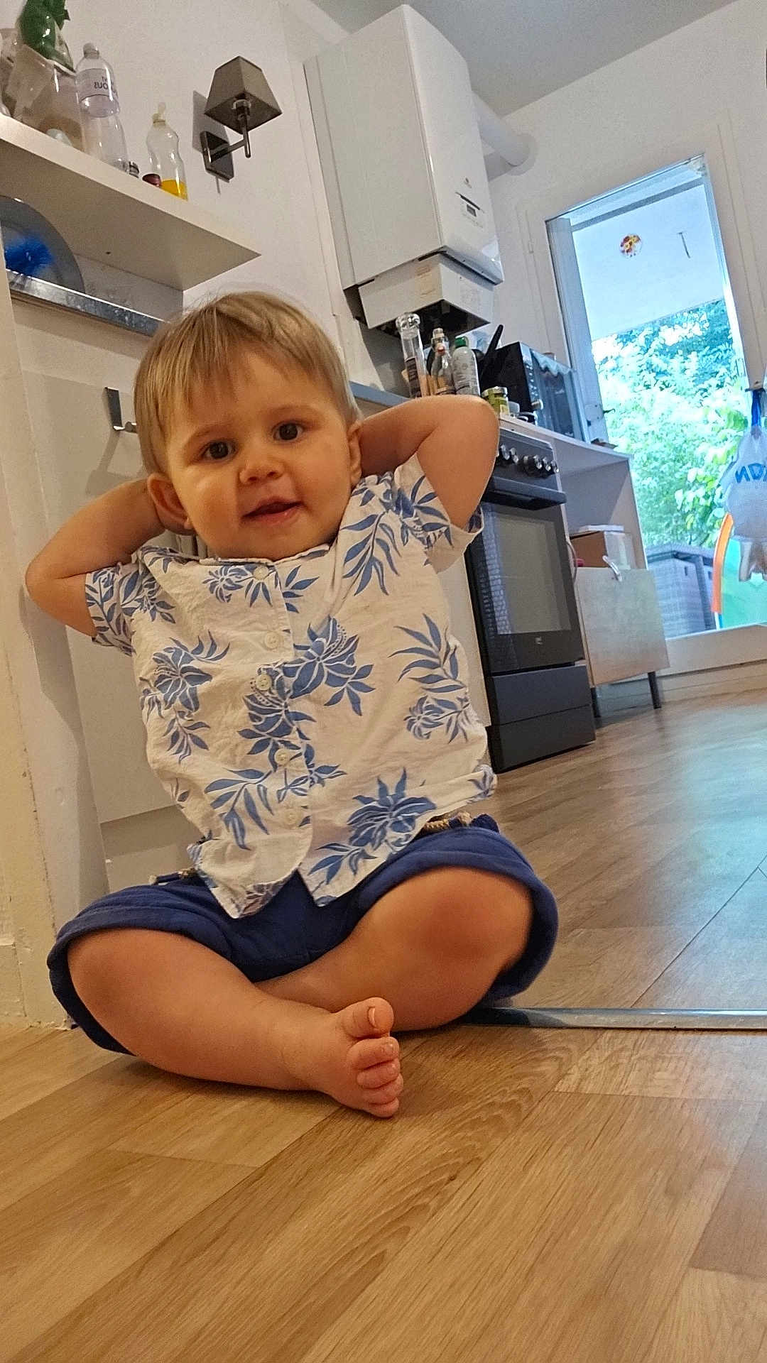 Lisandru participe au concours pour gagner de l'argent avec cette photo : toddler, child, floor, kitchen, shirt, shorts, barefoot, indoor, appliance, oven, door, window, wooden_floor, plant, relaxed, curious, home, casual, young_child, portrait