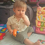 Lisandru participe au concours pour gagner de l'argent avec cette photo : toddler, child, toy, indoor, blanket, sitting, snack, clothing, face, hand, foot, shelf, books, colorful, plastic_toy, playtime, person, room, casual, curious