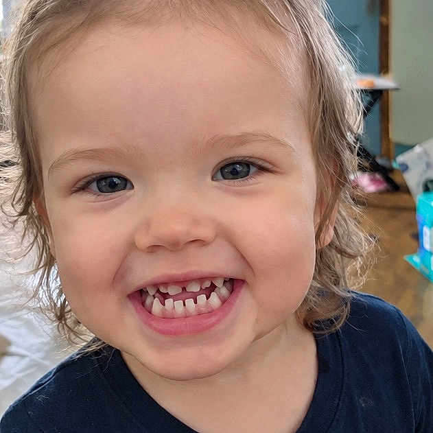 Elena is registered to the contest to win money with this photo: child, toddler, girl, smiling, grinning, portrait, close_up, face, teeth, bow, hair, blue_shirt, indoors, home, background, happy, cute, looking_at_camera, young_child, photography