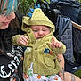 baby, infant, person, hoodie, dinosaur_costume, pacifier, tattoo, blue_hair, outdoor, stroller, leafy_background, cute, smile, winking, clothing, holding, nature, greenery, portrait, casual