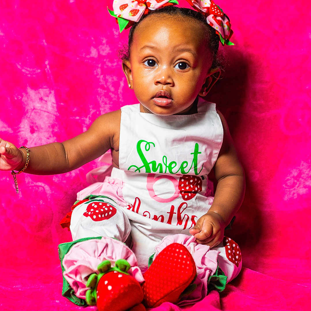 Jade joined the competition — help win amazing prizes! baby, child, infant, pink_background, strawberry_outfit, headband, bracelet, sitting, curious_look, portrait, cute, colorful, studio_photo, clothing, accessory, young_child, indoors, fashion, smiling, person