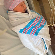 Gideon is registered to the contest to win money with this photo: newborn, baby, hospital, blanket, swaddled, sleeping, infant, cap, bed, bassinet, face, person, healthy, cute, resting, soft, peaceful, child, wrapped, indoors