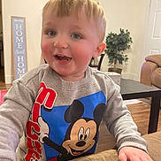 Kaiser joined the competition — help win amazing prizes! toddler, child, smiling, mickey_mouse, sweatshirt, indoor, living_room, couch, hand, face, blond_hair, person, happy, casual_clothing, furniture, plant, wood_floor, home_decor, cute, young_child