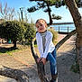 boots, cardigan, casual_clothing, child, daytime, greenery, nature, outdoor, park, pathway, person, portrait, relaxing, sea, sky, striped_clothing, sunlight, tree, water, young