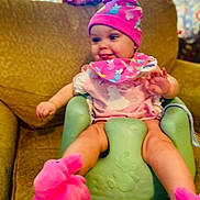 Reamonnee joined the competition — help win amazing prizes! baby, child, infant, hat, bib, pink, slippers, plush, green_baby_seat, couch, living_room, smiling, cute, indoor, person, clothing, seated, home, playful, colorful