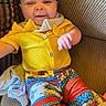 Reamonnee is registered to the contest to win money with this photo: baby, child, smiling, yellow_clothing, colorful_pants, patterned_pants, couch, striped_couch, indoor, happy, cute, playful, portrait, person, infant, seated, fabric, home, casual, young_child