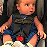 baby, car_seat, child, infant, blue_outfit, white_booties, seatbelt, strapped_in, wide_eyes, curious, indoors, sitting, young_child, clothing, footwear, person, portrait, baby_boy, car_travel, safety