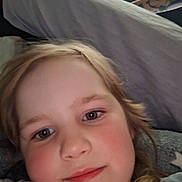 Sophia joined the competition — help win amazing prizes! child, face, selfie, close_up, smile, rosy_cheeks, blonde_hair, indoors, pillow, blanket, cozy, relaxed, casual, person, portrait, young, skin, eyebrows, head, comfort