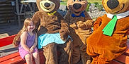 Sophia joined the competition — help win amazing prizes! child, girl, smiling, costume, mascot, bear, bench, outdoor, sunlight, wooden_floor, building, blue_sky, greenery, field, happy, daytime, purple_clothing, casual, fun, playful