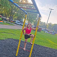 Ava is registered to the contest to win money with this photo: child, playground, climbing, ladder, smiling, barefoot, outdoor, grass, trees, sunlight, park, vehicle, casual_clothing, happy, summer, recreation, play, fun, daytime, nature