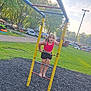 child, playground, ladder, barefoot, pink_top, black_shorts, outdoor, grass, trees, park, sunlight, play, climbing, summer, daytime, fun, person, recreation, casual, happy