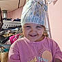 Violet is registered to the contest to win money with this photo: toddler, child, smiling, diaper, pink_shirt, indoor, clutter, clothes, household_items, face, happy, messy_room, portrait, person, cute, funny_hat, wall, curtain, jewelry, casual