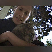 Smokey is registered to the contest to win money with this photo: person, girl, cat, pet, selfie, outdoor, trees, smile, face, arm, holding, porch, evening, whiskers, fur, animal, nature, casual, portrait, close_up