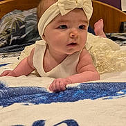 Aria a rejoint le concours — aidez-le/la à gagner de superbes lots ! baby, bed, bedding, blanket, bow, cheeks, cute, dress, eyes, face, hands, headband, indoor, infant, lying_on_stomach, pillow, portrait, purple_wall, toes, wooden_headboard