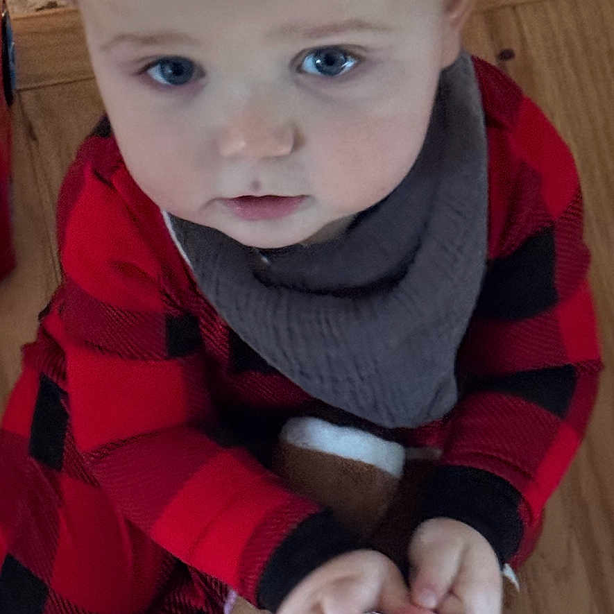 Lorenzo is registered to the contest to win money with this photo: baby, child, plush_toy, reindeer, red_pajamas, black_pajamas, blue_eyes, wooden_floor, indoors, hands, face, clothing, cute, infant, young_child, sitting, toy, expression, floor, looking_up