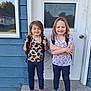 children, backpacks, door, house, concrete, step, blue_wall, smiling, standing, casual_clothing, patterned_shirts, shoes, outdoor, person, young, two_people, happy, childhood, daylight, siblings