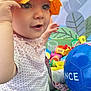 Lyse participe au concours pour gagner de l'argent avec cette photo : toddler, child, yellow_helmet, blue_ball, toys, play, indoor, cute, colorful, polka_dot_shirt, patterned_pants, smiling_face, curious, baby, hand, sitting, background_art, plastic_toys, green_surface, fun