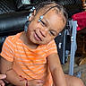 Shaun is registered to the contest to win money with this photo: toddler, child, braided_hair, beads, orange_shirt, striped_clothing, smiling, indoor, chair, leather_sofa, wooden_furniture, happy, person, portrait, cute, sitting, playful, home, young_child, casual_clothing