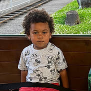 Shaun joined the competition — help win amazing prizes! child, toddler, curly_hair, mickey_mouse, shirt, red_pants, bench, seat, green_chair, window, outdoor, railway_track, grass, plants, fence, car, serious_expression, portrait, indoors, casual_clothing