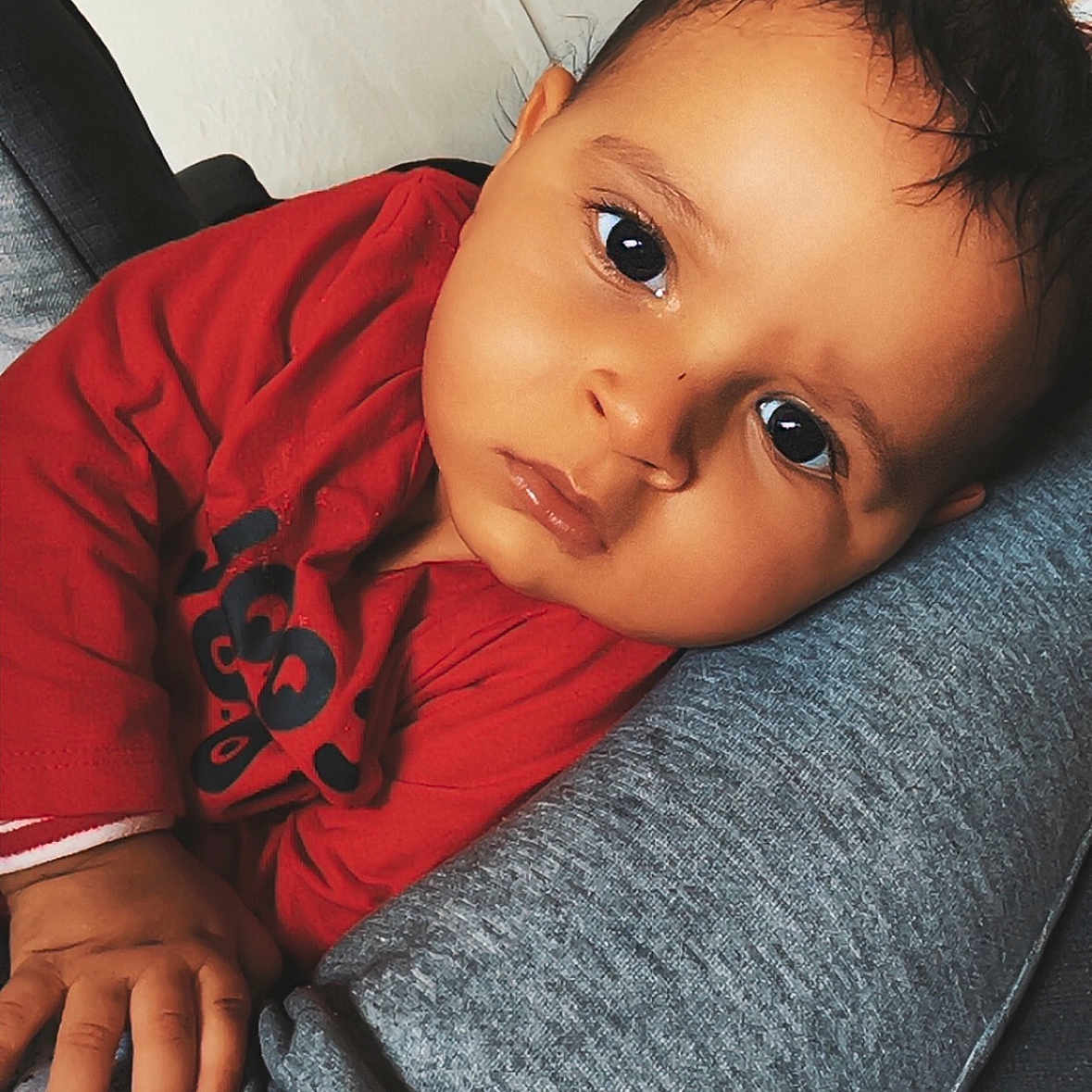 Naël participe au concours pour gagner de l'argent avec cette photo : baby, casual_clothing, child, closeup, cushion, cute, expression, eyes, face, hand, head, indoor, infant, lying_down, person, portrait, red_shirt, resting, skin, young