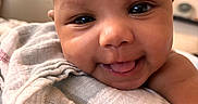 Mulahn joined the competition — help win amazing prizes! baby, close_up, smile, tongue_out, blanket, face, skin, indoor, person, infant, cute, happy, child, portrait, soft_texture, warm_light, head, expression, young, wrapped