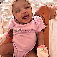 Mulahn joined the competition — help win amazing prizes! baby, infant, smile, purple_onesie, mittens, tattoo, leg, bed, blanket, person, happy, cute, indoor, skin, handwear, headwear, expression, sitting, cozy, comfort