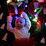 baby, infant, holiday_lights, christmas_decorations, festive, red_bow, blanket, pattern, christmas_tree_pattern, toddler, celebration, indoors, cute, smiling, happy, face, person, holiday, colorful_lights, fun