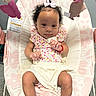 baby, infant, child, pink, bow, curly_hair, floral_pattern, socks, baby_rocker, toy, carpet, bracelet, white_clothing, cute, portrait, indoor, seat, happy, skin, person